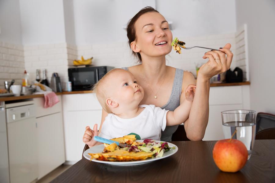 Mutter mit Baby auf dem Schoß beim Essen, babygeleitete Beikost